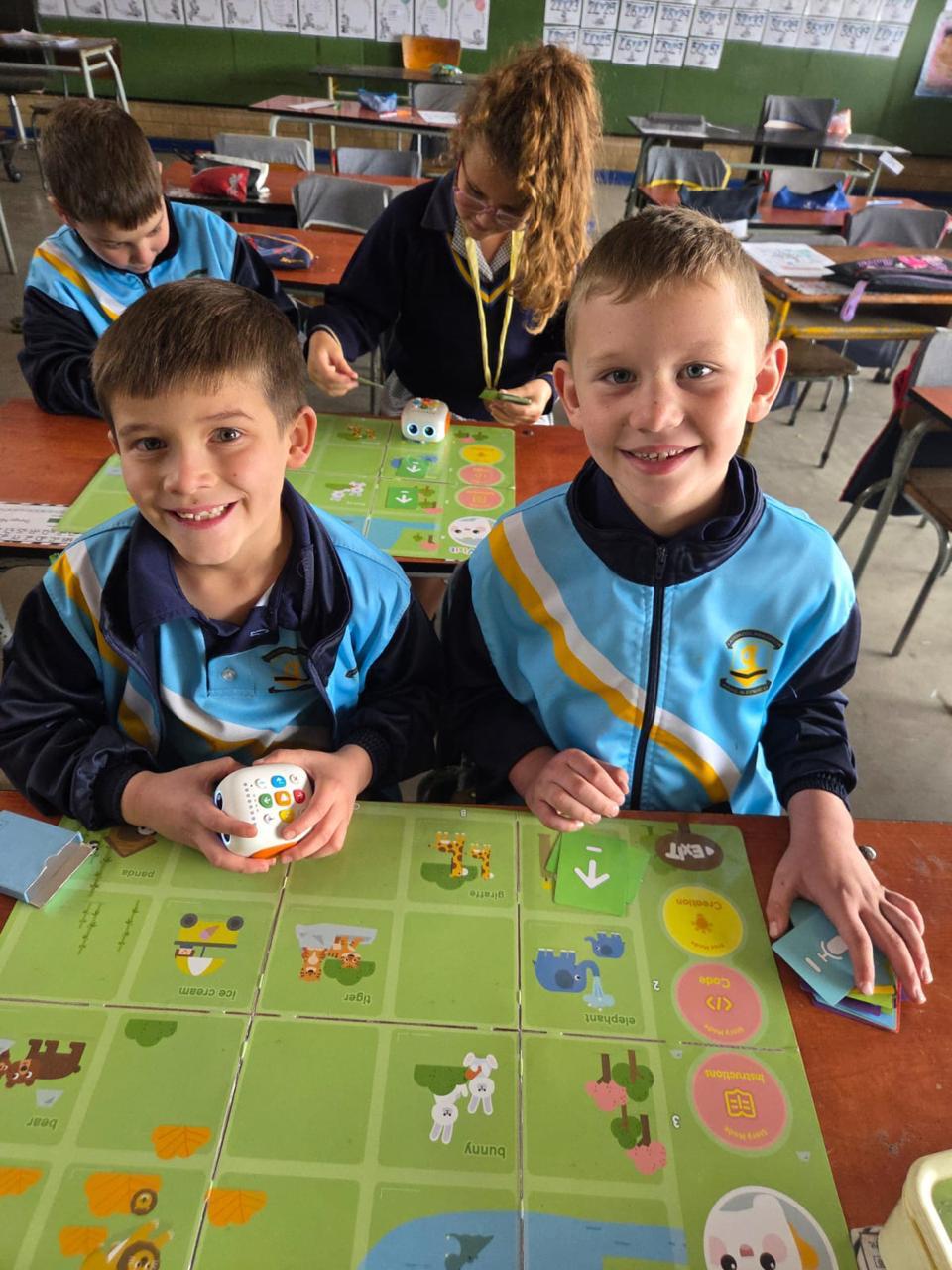 Two boys in classroom using a programmable coding robot with a game board