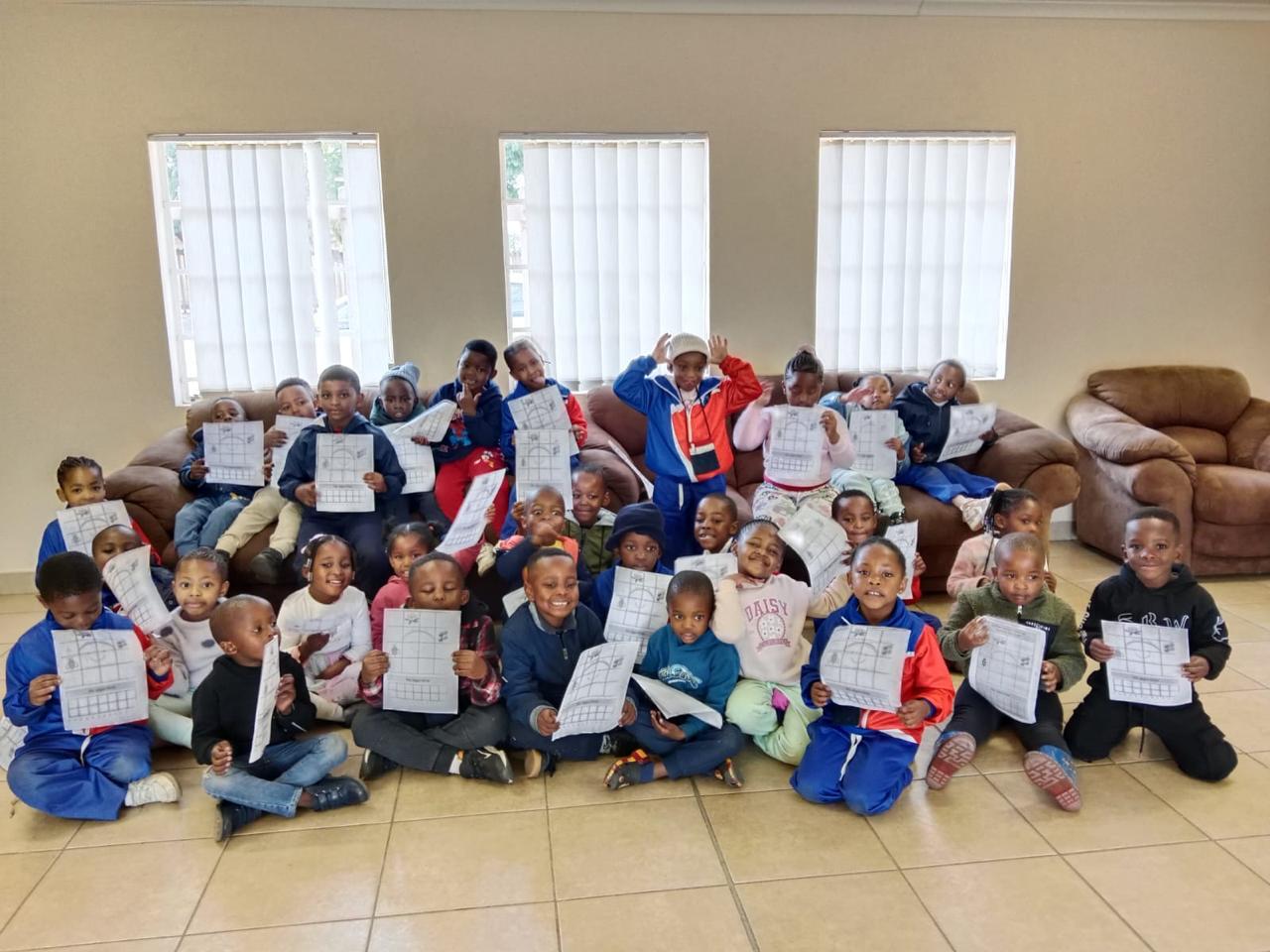 Large group of young learners proudly holding up their coding worksheets
